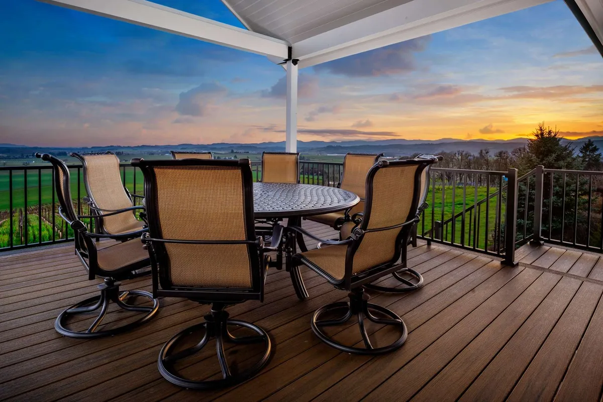 A stylish exterior dining space with a table and swivel chairs, positioned to maximize views of a vibrant sunset and distant mountains. The setting is intimate and inviting, ideal for quiet mornings or celebratory gatherings alike.