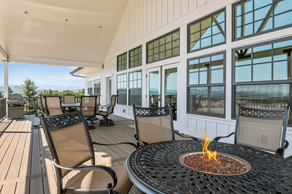 A cozy outdoor seating area surrounding a modern gas fire pit, with comfortable chairs arranged for conversation. Beyond the fire pit, rolling hills and a sweeping mountain view set a tranquil, inviting backdrop, hinting at sunset or twilight ambiance.