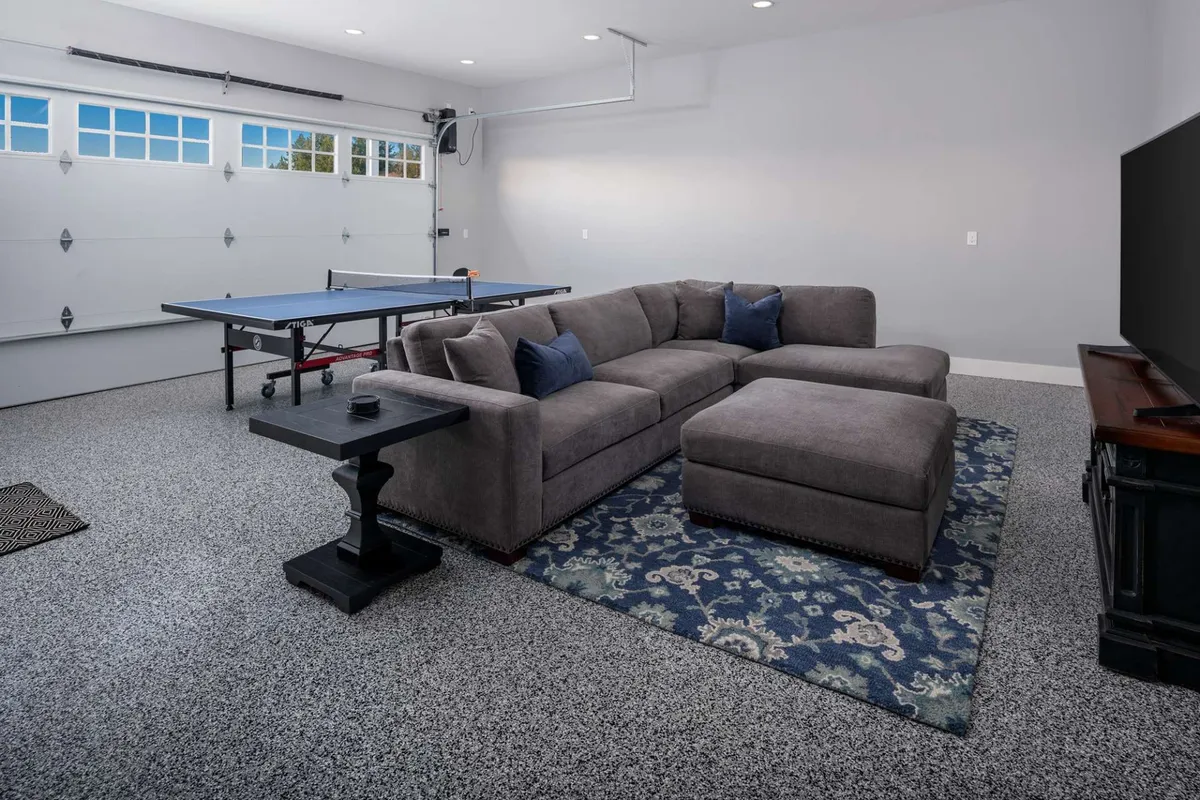 A vibrant recreation room featuring a competition-level ping-pong table as the centerpiece, flanked by a plush sectional sofa and a large HD television mounted on the wall. The space is designed for both action-packed games and relaxation, with cozy lighting and inviting decor that encourages friendly gatherings.