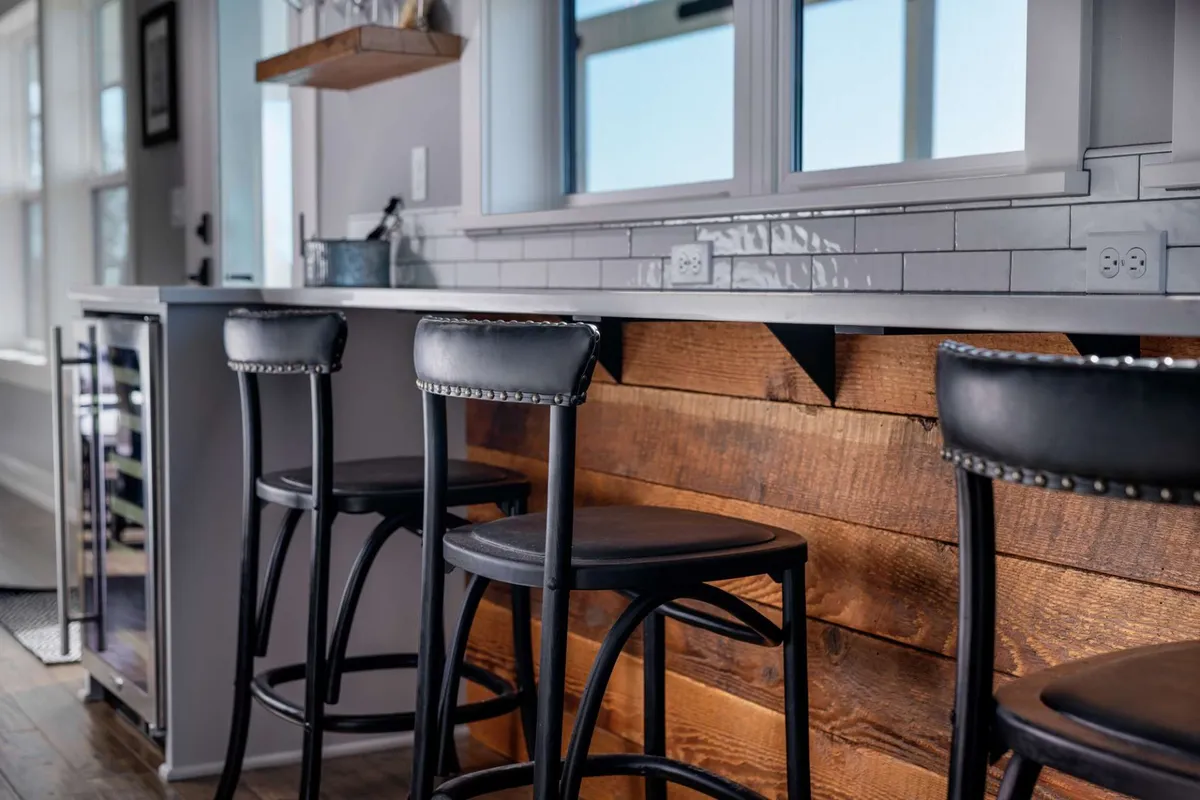 A warm and inviting kitchen with bar stools along a wooden counter and a large window letting in natural light. The setting is ideal for socializing, casual cooking sessions, or enjoying catered meals. Its approachable layout highlights the ease of hosting or simply relaxing in comfort.
