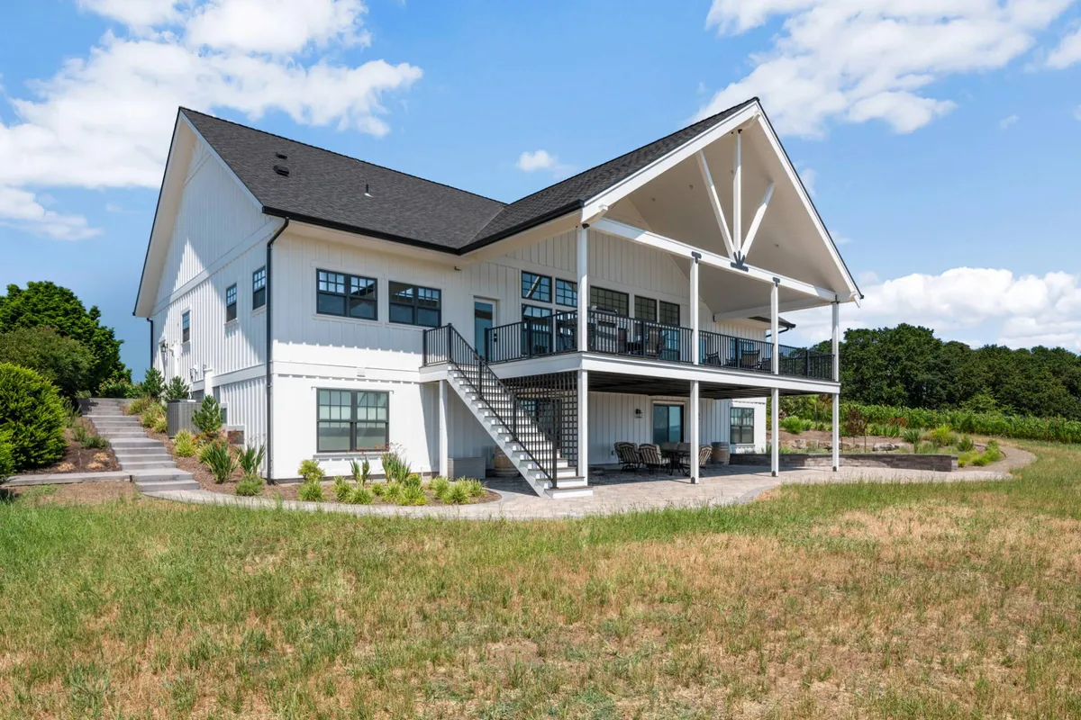 An exterior view highlighting the house’s spacious deck, surrounded by landscaped gardens and open space. The deck offers a natural extension of the indoor living areas, set against a serene backdrop of hills.